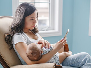 Mom sitting with baby in her arms looks at phone