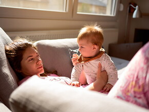 Moms lies on sofa, holding baby and looking dazed