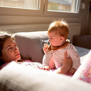 Moms lies on sofa, holding baby and looking dazed Moms lies on sofa, holding baby and looking dazed