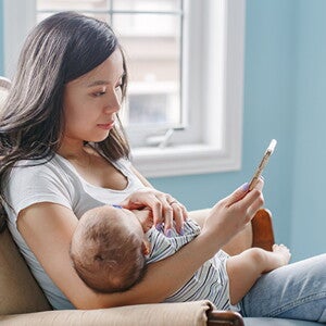 Mom sitting with baby in her arms looks at phone Mom sitting with baby in her arms looks at phone